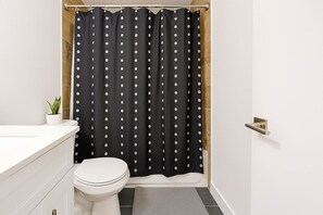A bathroom with a white toilet, a black shower curtain with white polka dots, a small potted plant, and a white sink. - 2BR Calm & Aesthetic Apt (Chicago)