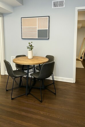 A room with a round wooden table, four black chairs, a potted plant, and a framed abstract artwork on the wall. - 2BR Calm & Aesthetic Apt (Chicago)