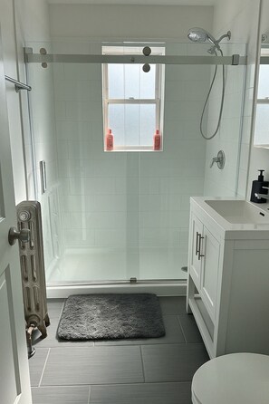Une salle de bain moderne avec une douche à parois de verre, une fenêtre, un lavabo blanc et des toilettes.