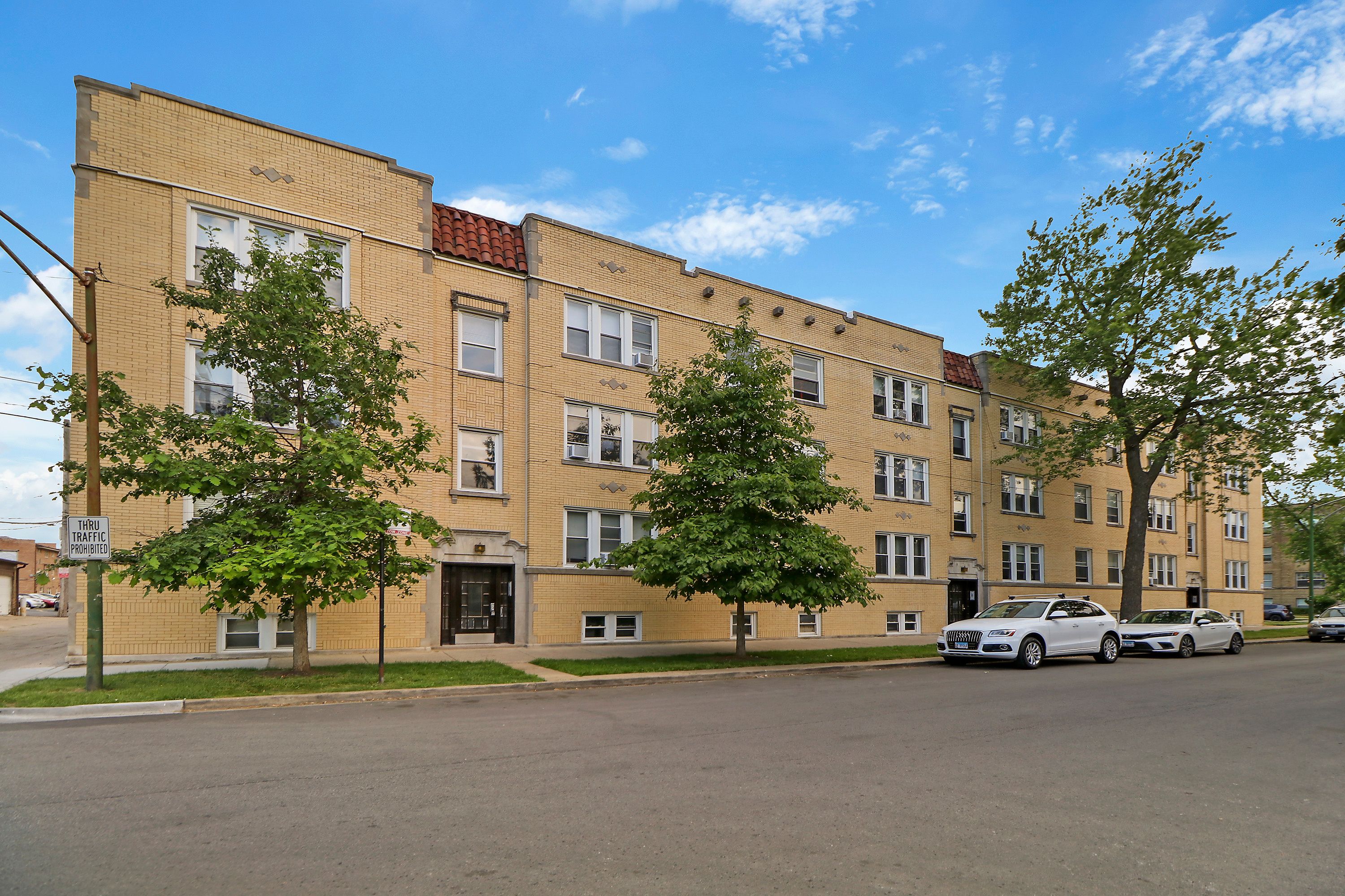 A multi-story apartment building with a brick facade, several windows, and a few trees in front.