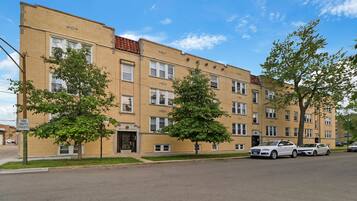 A multi-story apartment building with a brick facade, several windows, and a few trees in front.