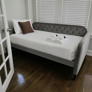 A single bed with a grey upholstered headboard, white bedding, and two rolled towels.