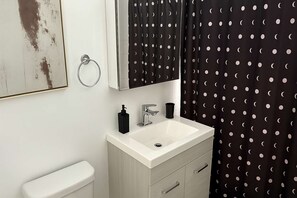 Un bagno con un lavandino bianco, uno specchio e una tenda da doccia con pois neri e bianchi.