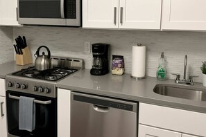 Una cucina moderna con elettrodomestici in acciaio inossidabile, tra cui piano cottura, forno e lavastoviglie. Ci sono pensili, un forno a microonde e una macchina da caffè sul piano di lavoro.