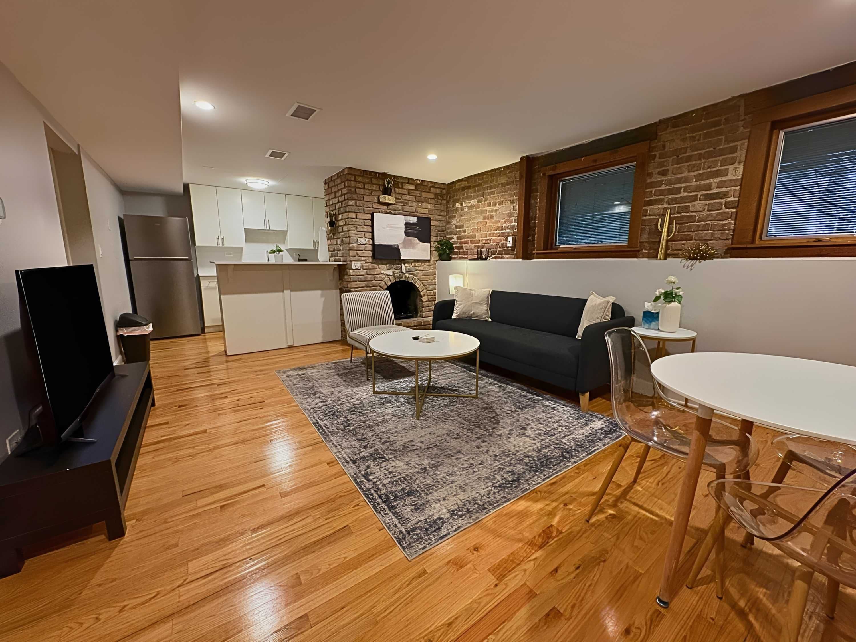 A modern living space with a kitchen, a black sofa, a round coffee table, and a dining area with a glass table and chairs.