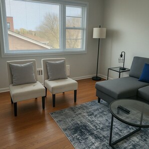 A living room with a sofa, two armchairs, a coffee table, a lamp, and a view of a building outside.