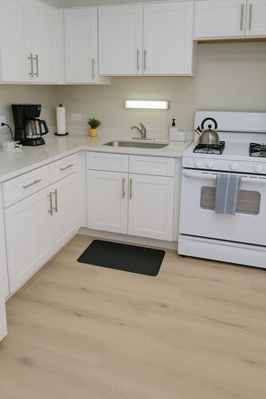 A modern kitchen with white cabinets, a stainless steel sink, a stove, and a coffee maker.