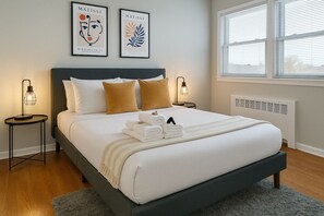 A neatly made bed with white and beige bedding, two wall-mounted artworks, and bedside lamps. - Chill & Cozy 2BR Apt | Walk to Parks, Food & More! (Chicago)