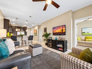 A modern living room with a sofa, ottoman, and a coffee table. There is a kitchen area in the background with cabinets and a dining table. - Luxury Living at the The Cays! Resort Pool/Spa, Steam, Gym. Waterfront Community! (Chandler)