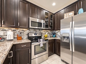 A modern kitchen with dark wood cabinets, stainless steel appliances, and a tiled backsplash. - Luxury Living at the The Cays! Resort Pool/Spa, Steam, Gym. Waterfront Community! (Chandler)