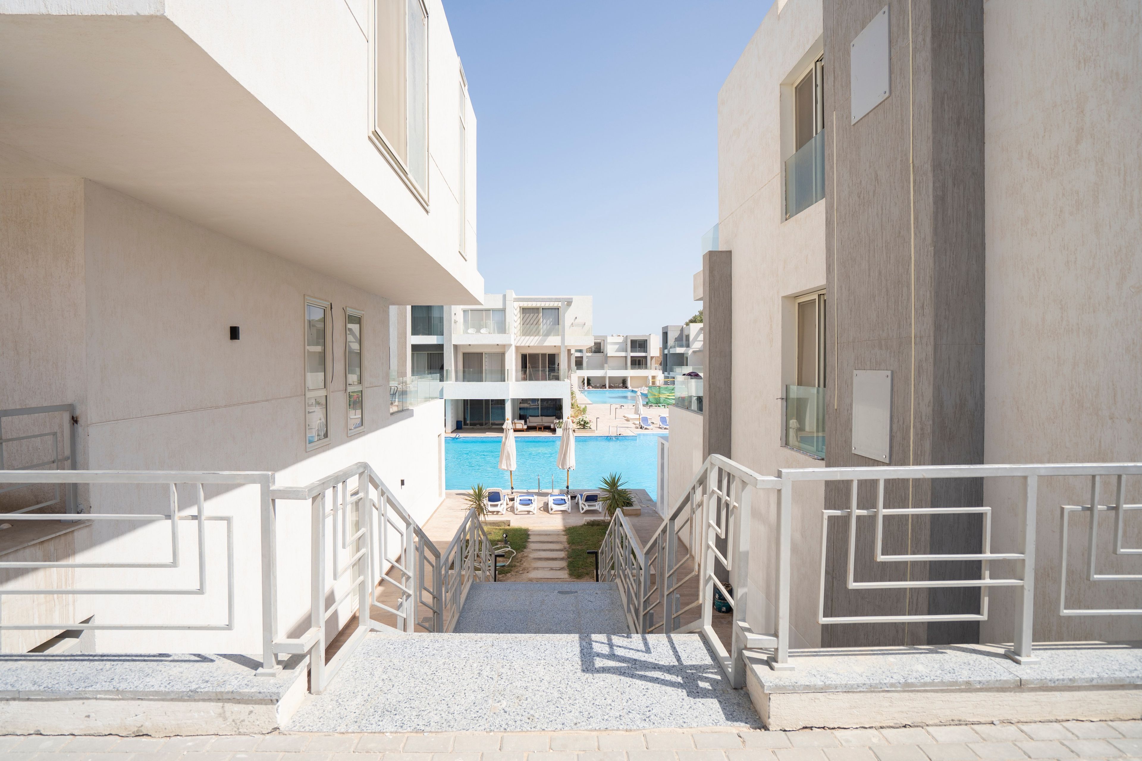 A modern hotel with a pool area, multiple balconies, and a clear sky.