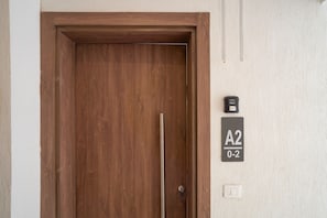 En trædør med nøglehul og dørgreb. Til højre er der en lyskontakt på væggen og et nummerskilt med teksten 'A2 0-2'.