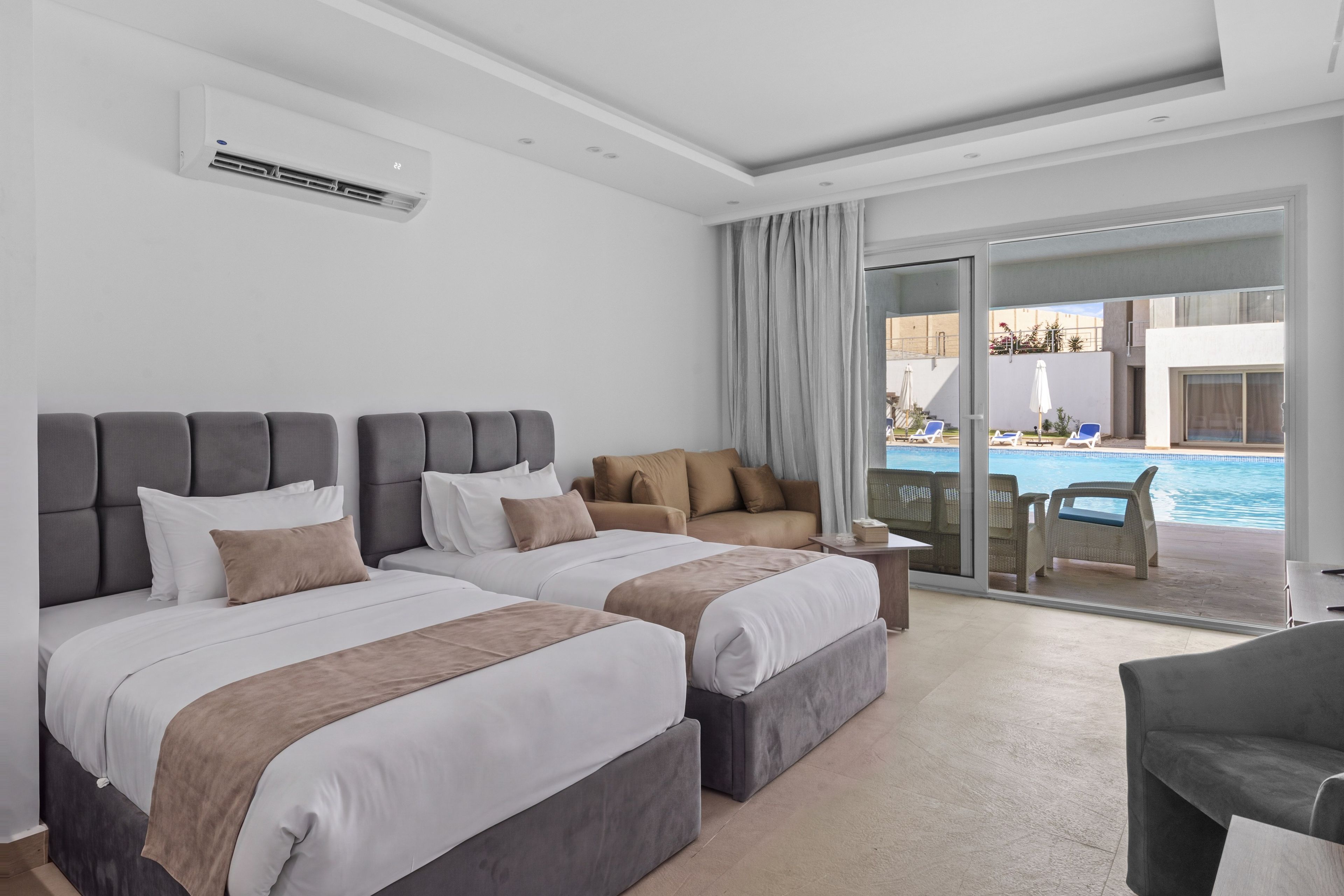 Et hotelværelse med to senge, en sofa, et lille bord og udsigt til en pool.
