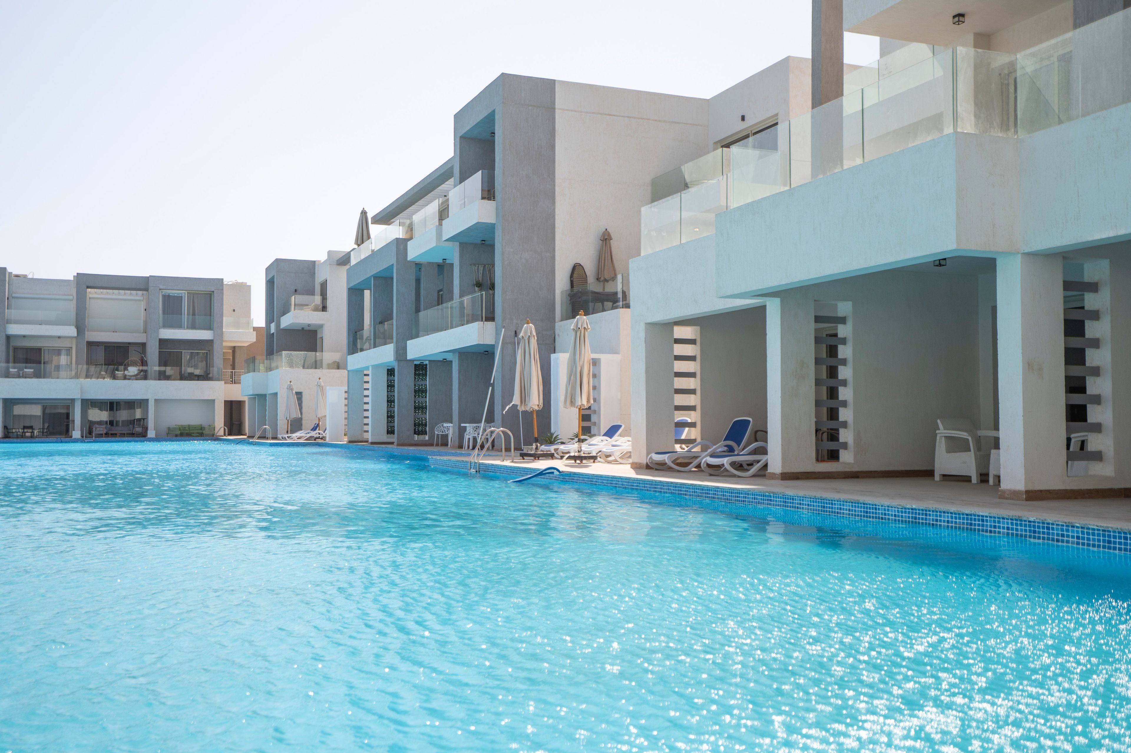 Ein Swimmingpool mit Liegestühlen und Sonnenschirmen, umgeben von modernen Gebäuden mit Balkonen.