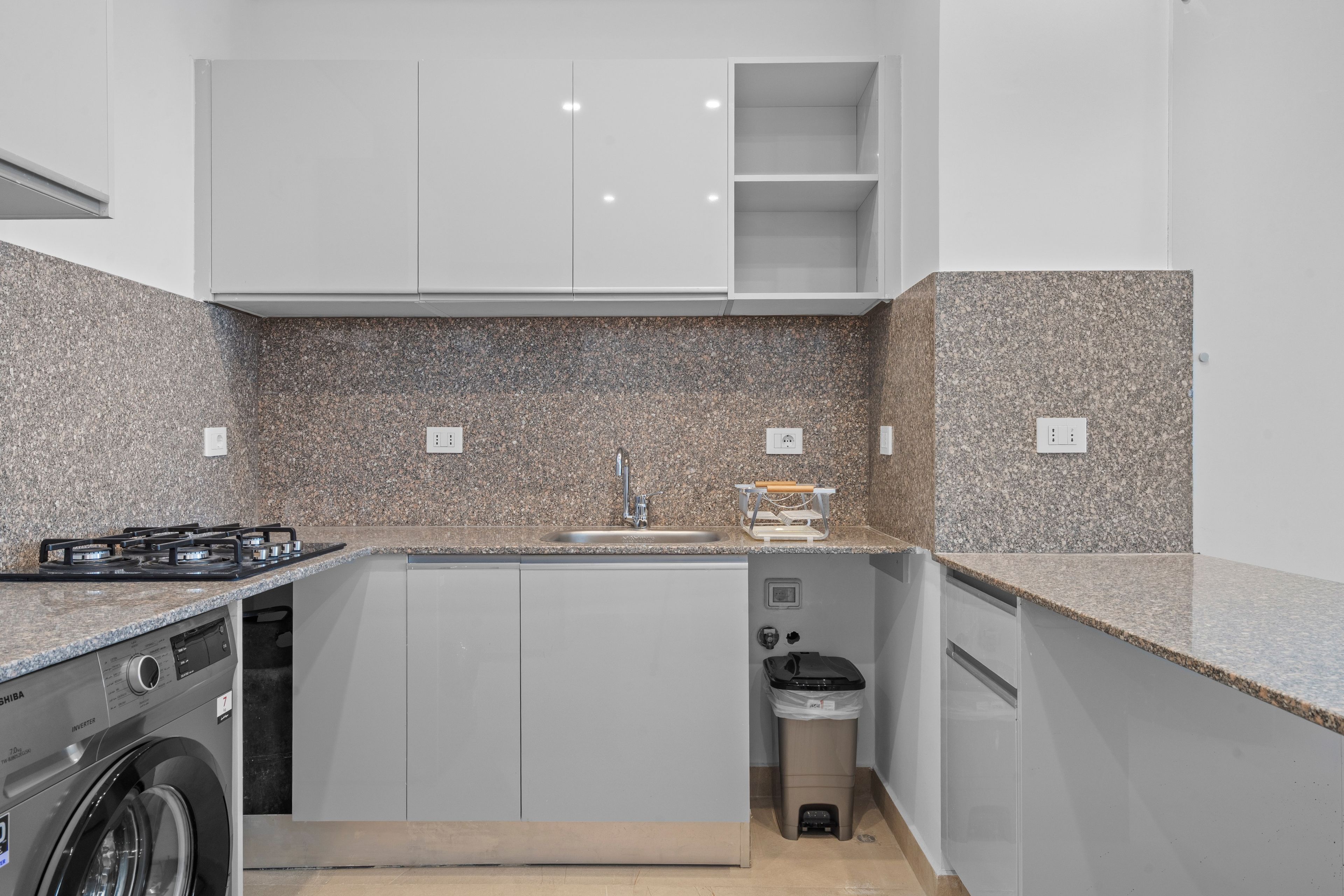 A compact kitchen with a built-in washer, a sink, and a trash bin.