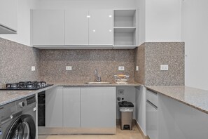 Una cocina compacta con lavadora integrada, un lavamanos y un cubo de basura.