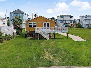 A two-story house with a deck and a small porch, surrounded by a grassy yard and other houses. - Gulf View, Walk to the Beach (Galveston)