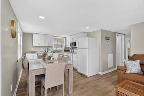 A modern kitchen with white appliances, a dining area with a table and chairs, and a living room with a sofa and a coffee table. - Gulf View, Walk to the Beach (Galveston)