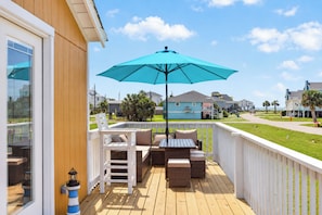 A wooden deck with outdoor furniture, a blue umbrella, and a view of neighboring houses. - Gulf View, Walk to the Beach (Galveston)