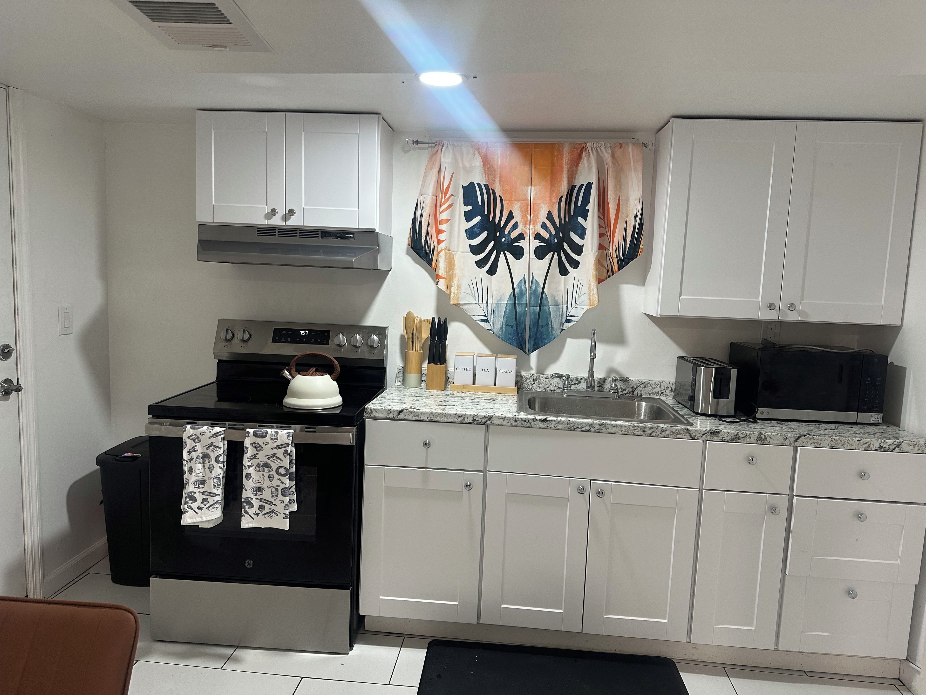 A compact kitchen with a stove, microwave, sink, and white cabinets.