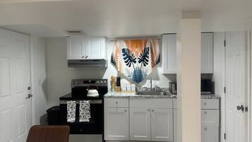 A compact kitchen with white cabinets, a black stove, and a stainless steel sink.