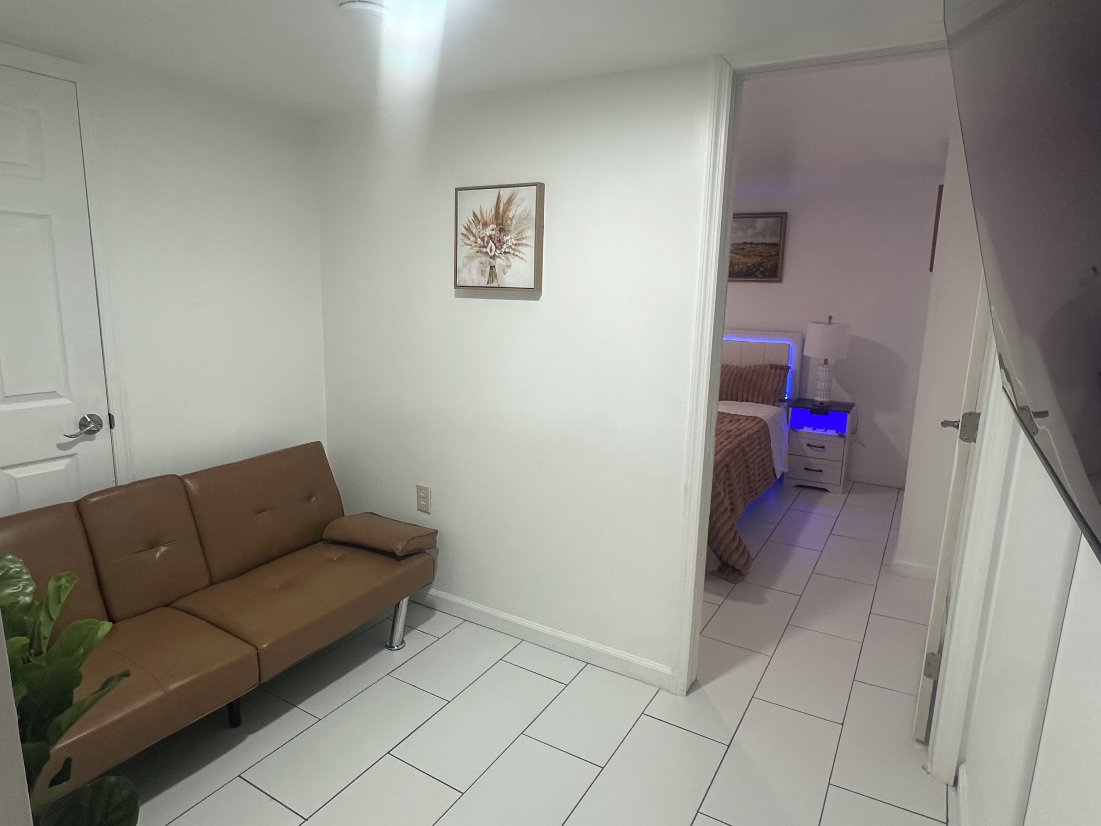 Une pièce avec un canapé marron, un lit doté d’une tête de lit illuminée en bleu et un tableau accroché au mur.
