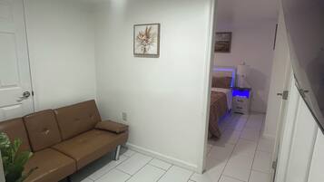 Une pièce avec un canapé marron, un lit doté d’une tête de lit illuminée en bleu et un tableau accroché au mur.