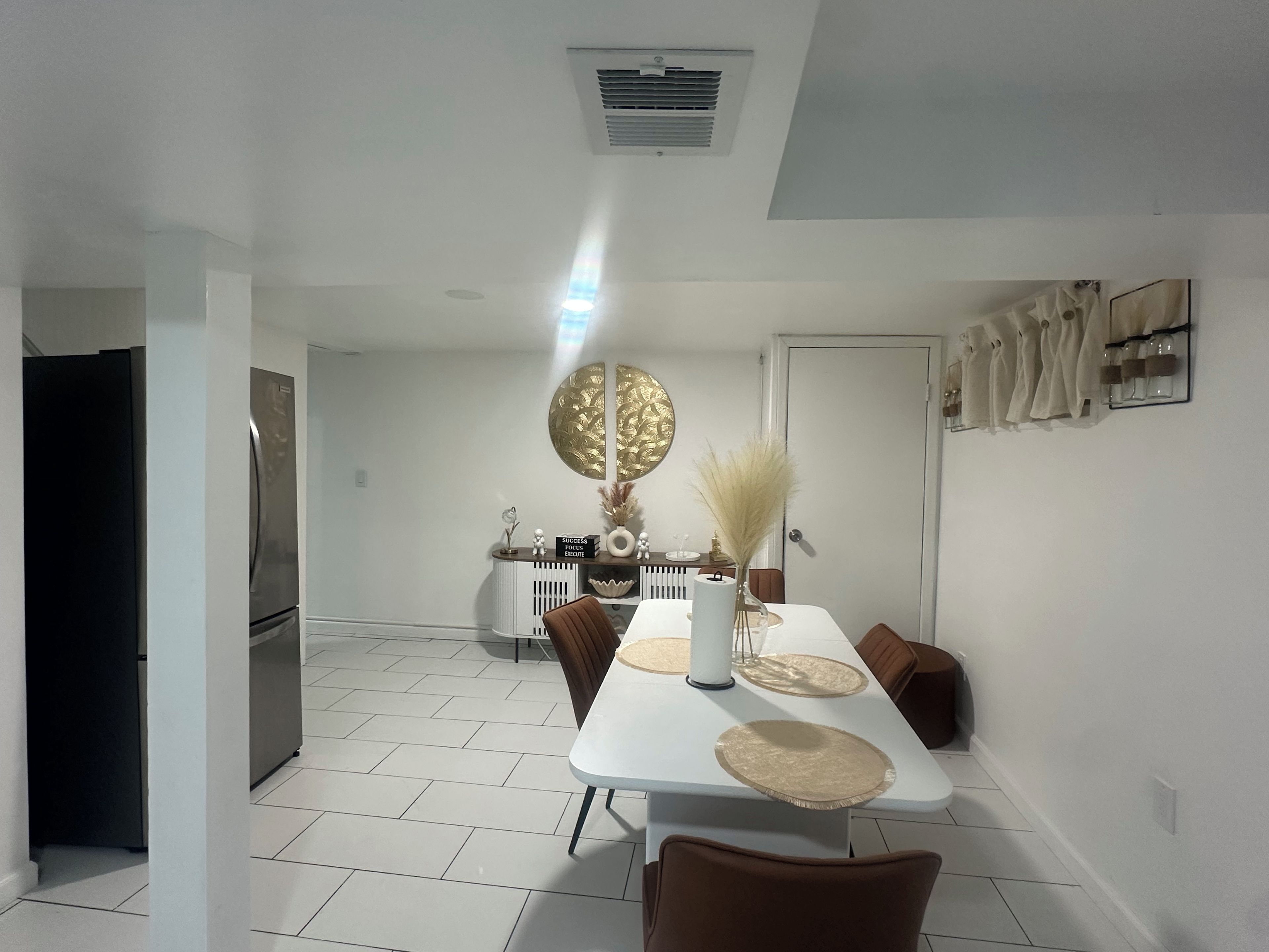 A modern dining area with a white table, brown chairs, and a decorative wall piece.