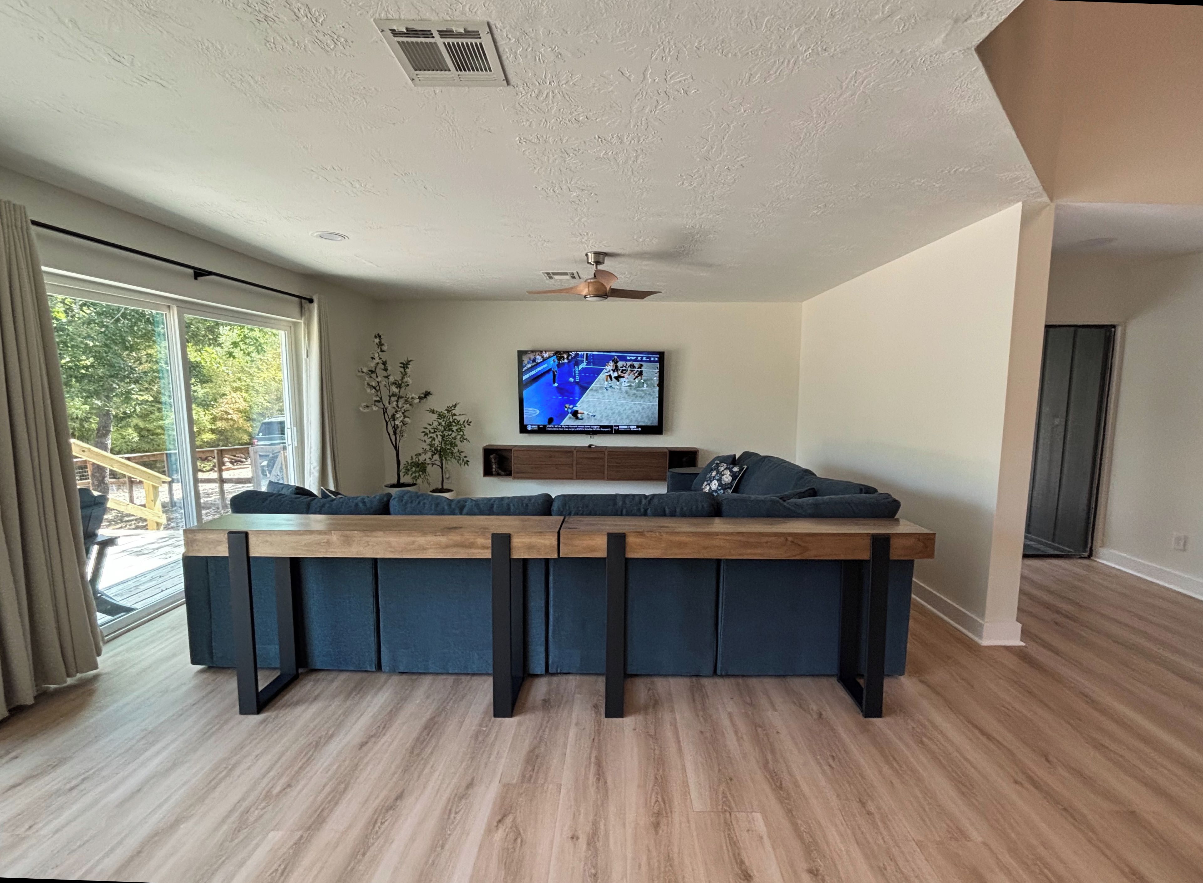 A modern living room with a wooden coffee table, a flat-screen TV, and a ceiling fan.