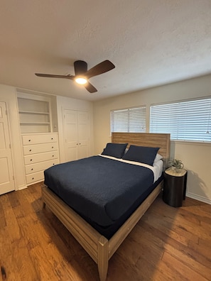 A bedroom with a bed, a ceiling fan, a window with blinds, and a built-in wardrobe.