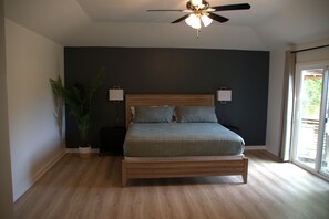 A bedroom with a bed, ceiling fan, potted plant, and a view through a window.
