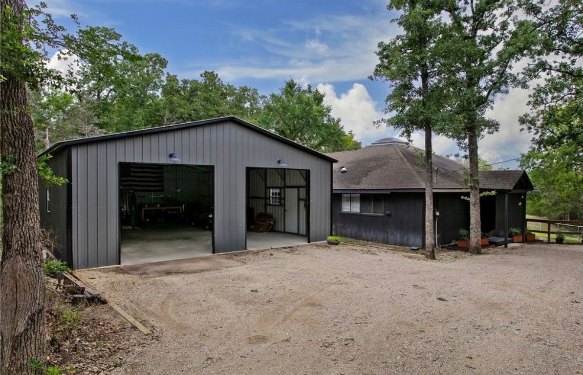 A two-story building with a garage and a covered area, surrounded by trees.