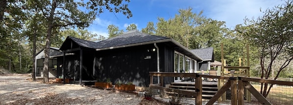 A black cabin with a wooden deck and a fenced area.