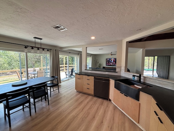A modern kitchen with a dining area, large windows, and a view of the outdoors.