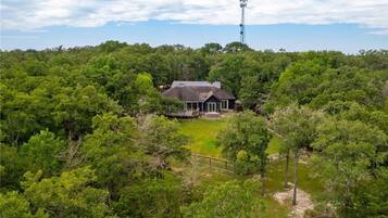 Une maison entourée d’une forêt dense, sous un ciel dégagé.