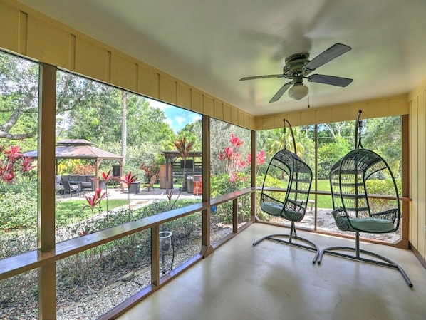A covered patio with two chairs, a ceiling fan, and a view of a garden and outdoor furniture. - Tremendous house with AC in sunny Vero Beach (Vero Beach)