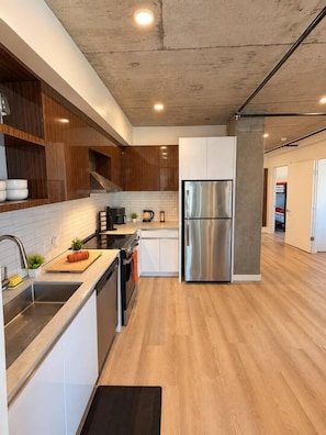 A modern kitchen with stainless steel appliances, wooden cabinets, and a concrete ceiling. - The Ember Retreat !! (San Diego)