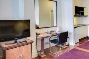 Une pièce de taille modeste équipée d’une télévision, d’un bureau, d’une chaise et d’une petite kitchenette.