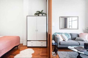 A bedroom with a wardrobe, a bed, a grey sofa, and a small table with a laptop. - Heritage Hotel 1 Bedroom Apartment ! (Auckland CBD)