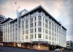 A multi-story hotel with a prominent entrance, large windows, and a flag on top. - Heritage Hotel 1 Bedroom Apartment ! (Auckland CBD)