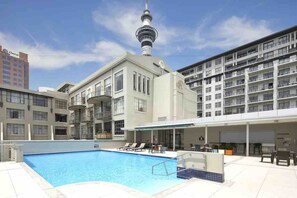 A hotel with a swimming pool, a covered area with seating, and a view of a tower. - Heritage Hotel 1 Bedroom Apartment ! (Auckland CBD)