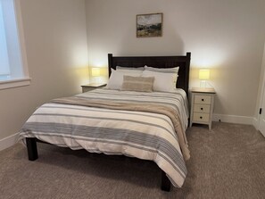 Un dormitorio con una cama, dos mesitas de noche, una lámpara y un cuadro en la pared.