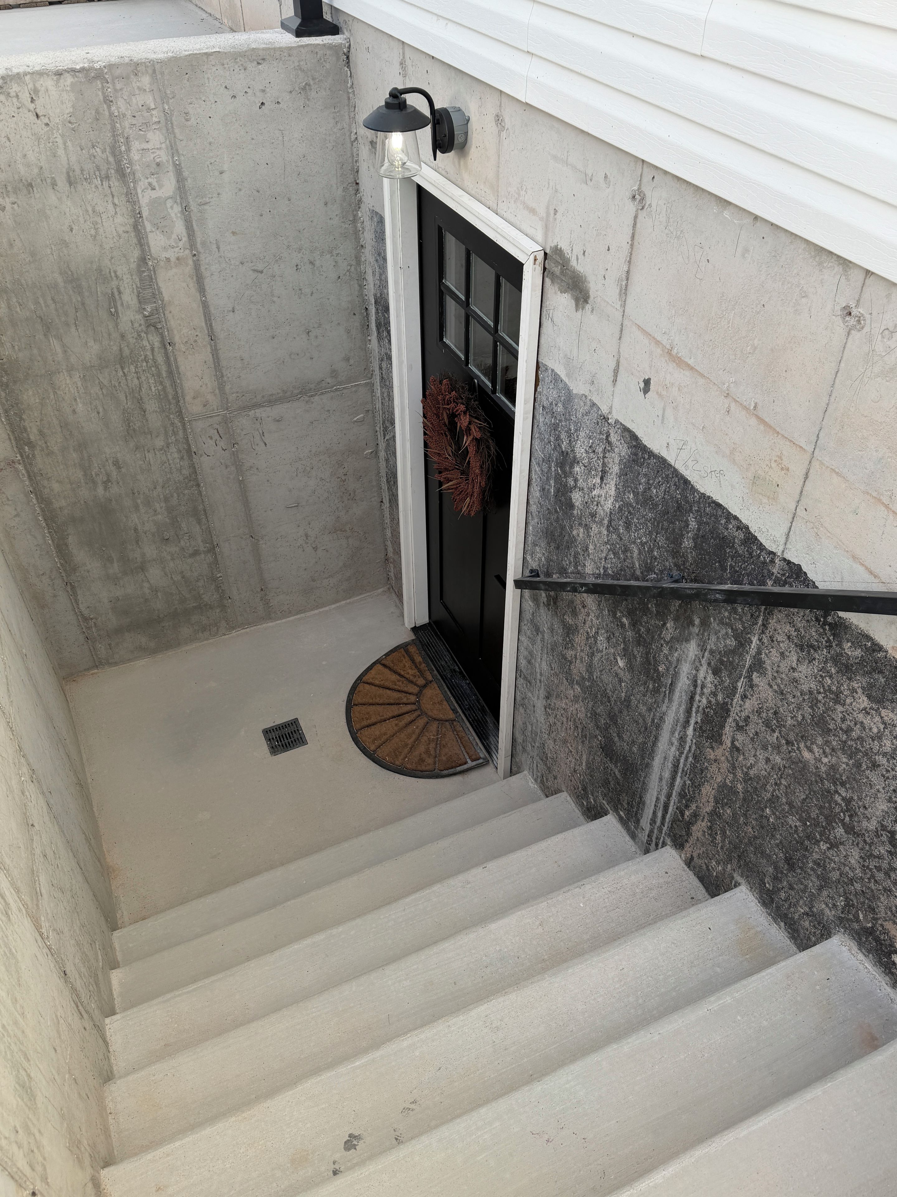 A concrete staircase with a door leading to a room, a doormat, and a light fixture above the door.