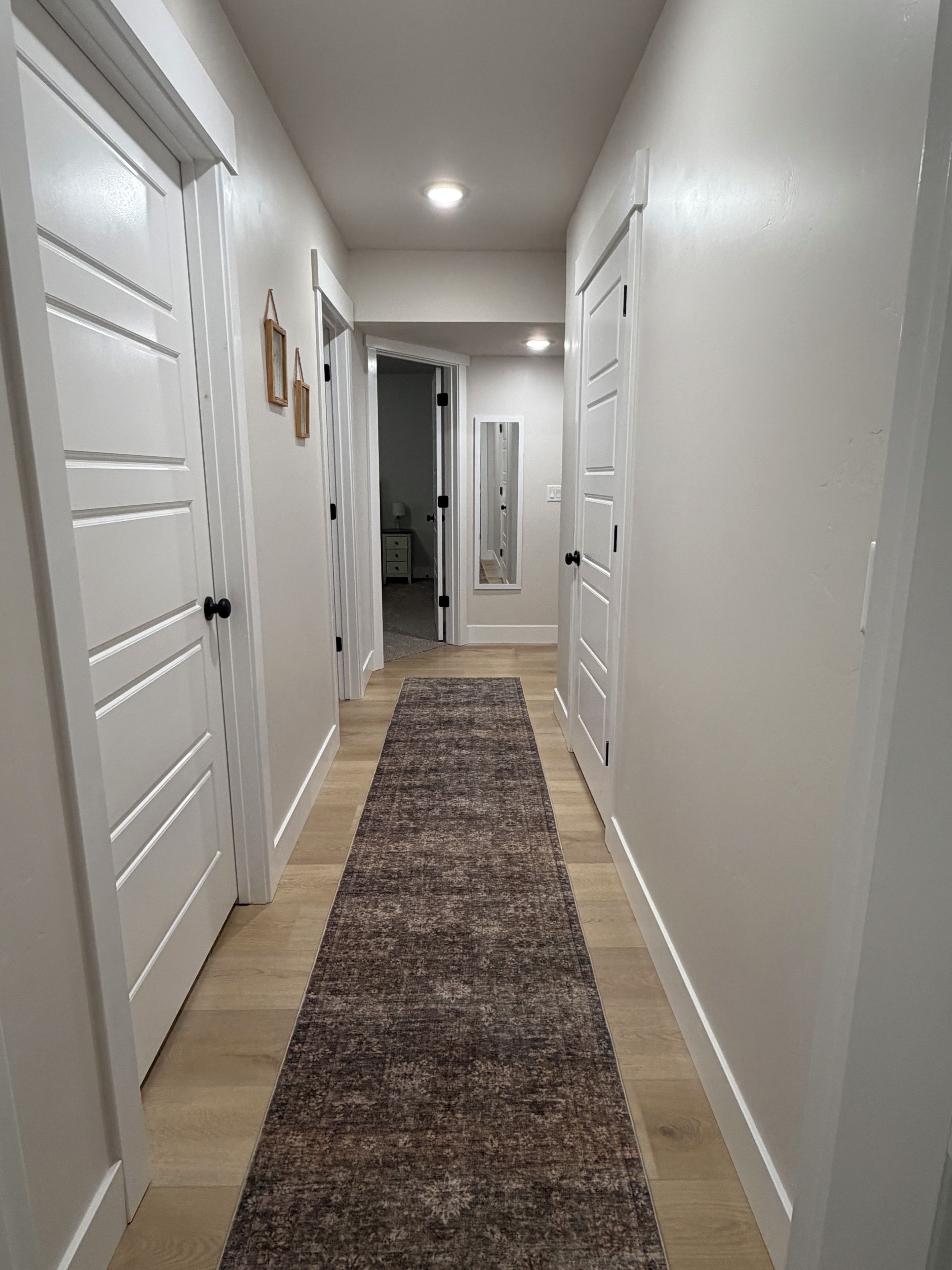 A hallway with white doors, a patterned rug, and a light-colored floor.