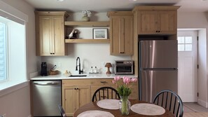 A modern kitchen with wooden cabinets, a stainless steel refrigerator, a built-in oven, and a dining table with chairs. - Just-Finished 2BR Basement Suite • Private Entrance (Ammon)