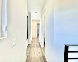 A hallway with a light-colored floor, white walls, and a door at the end. - 1 king 2 Queen beds Townhome (San Diego)