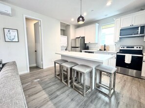 A modern kitchen with white cabinets, stainless steel appliances, and a bar stool seating area. - 1 king 2 Queen beds Townhome (San Diego)