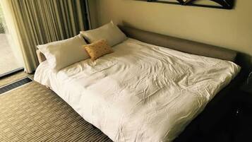 A neatly made bed with a patterned pillow, a bedside lamp, and a window with curtains.