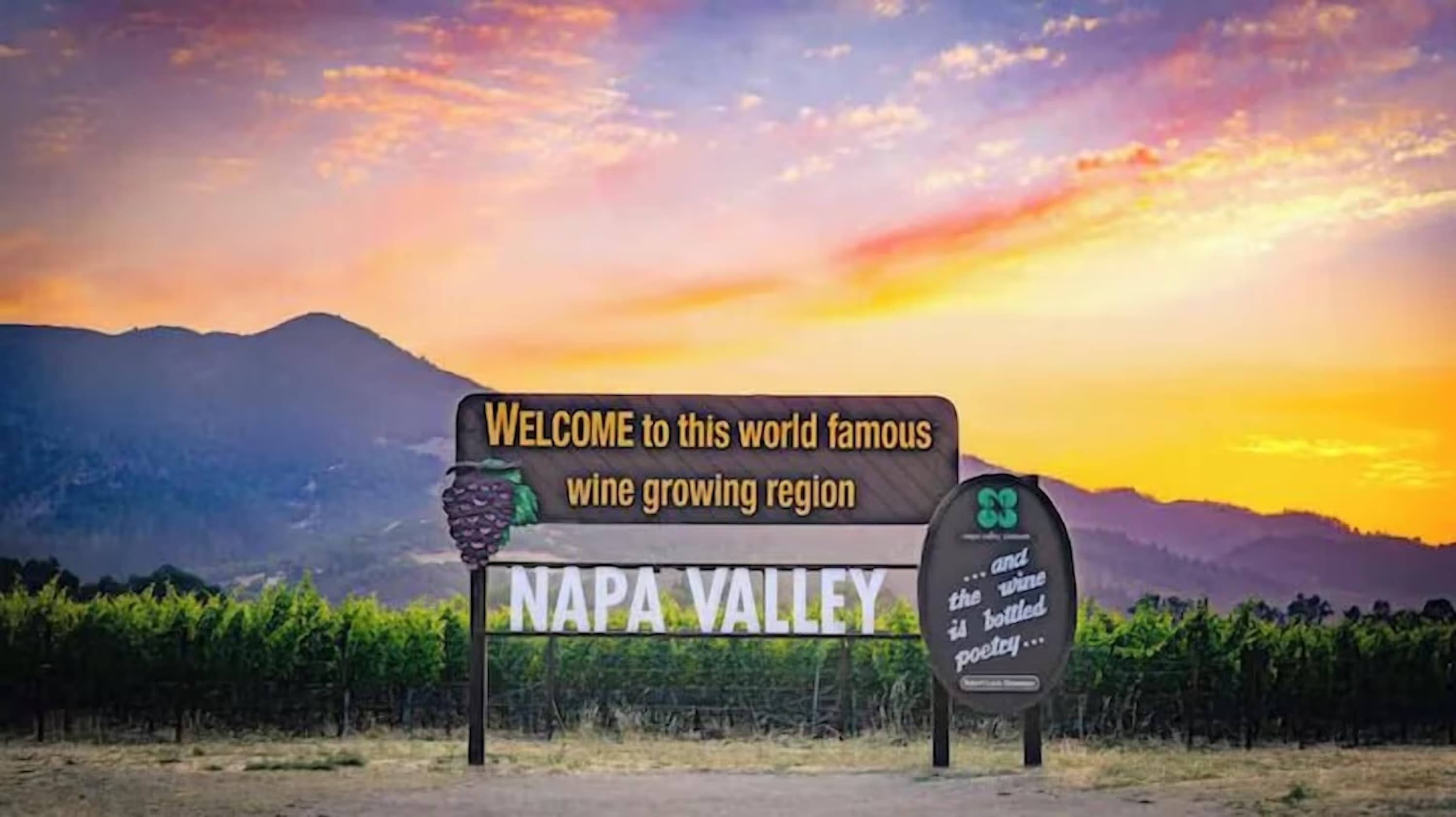 Un letrero de bienvenida a Valle de Napa, una región vinícola famosa, con viñedos y montañas de fondo.