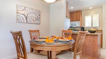Un coin repas avec une table ronde dressée pour quatre personnes, entourée de chaises en bois dotées d’assises rembourrées. Un tableau est accroché au mur, au-dessus de la table.